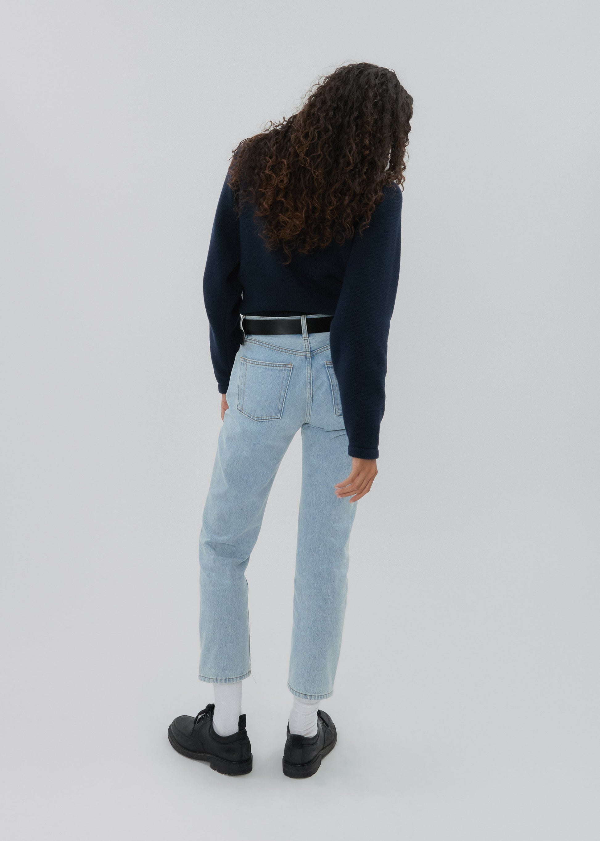 Person wearing light blue jeans and a dark long-sleeve top on a white background