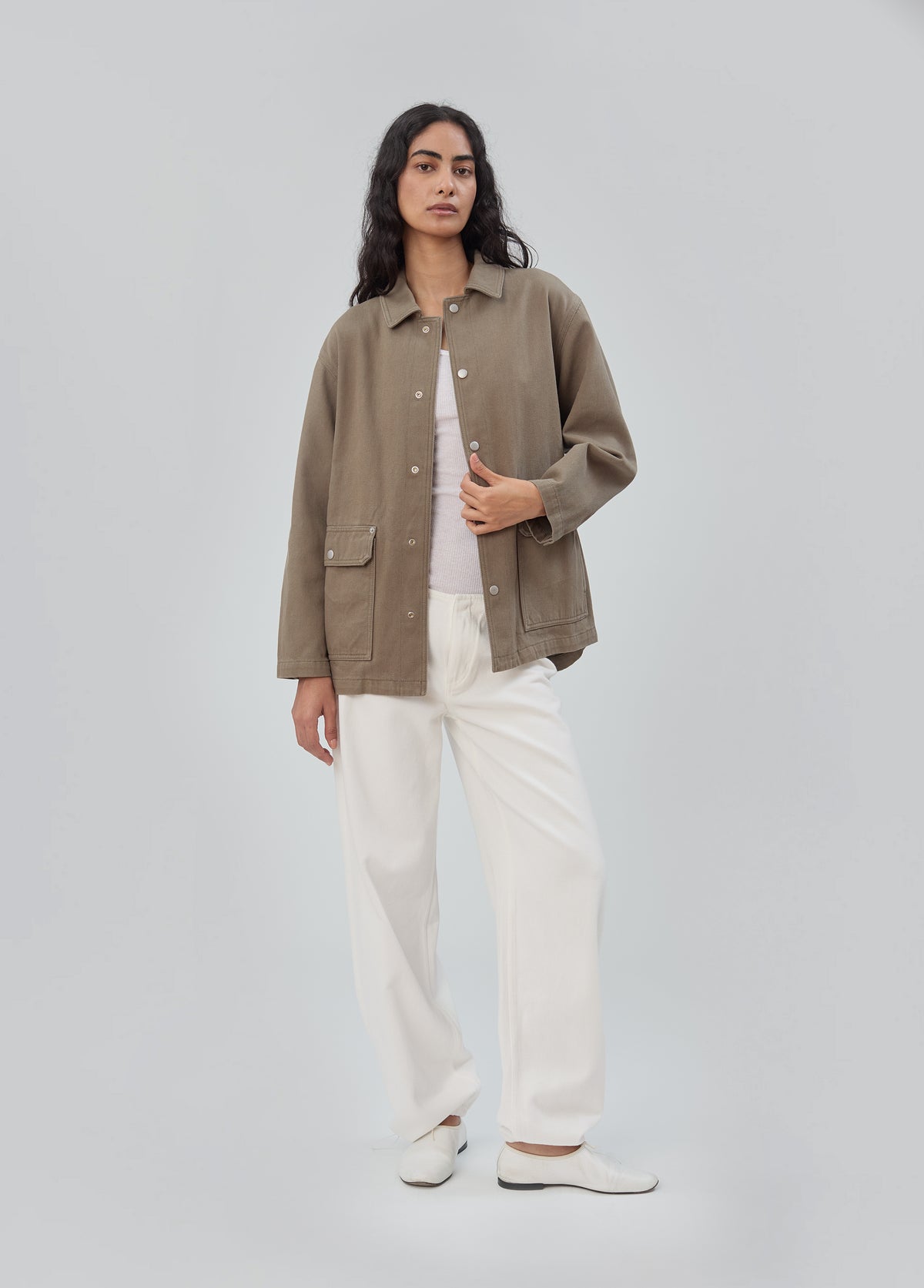 A person wearing an olive green Barn Jacket in Army Green over a white tank top and white trousers.