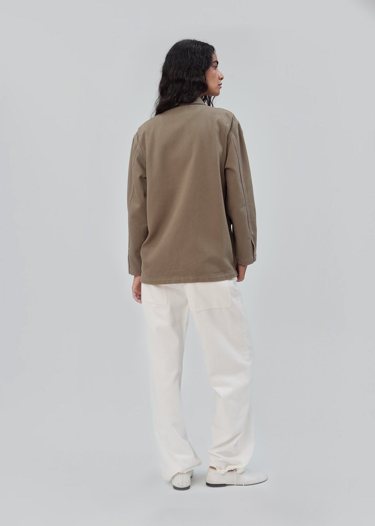 A person seen from behind wearing an olive green cotton Barn Jacket in Army Green and white trousers.