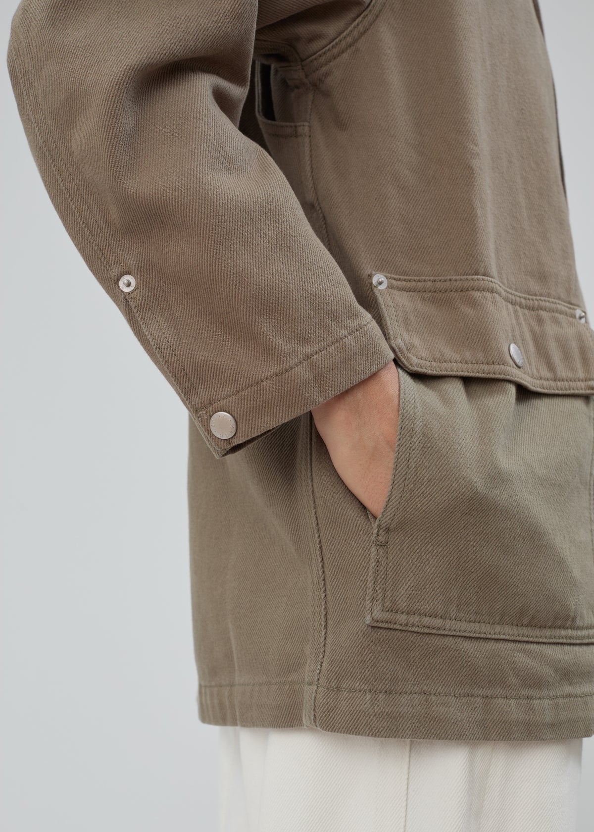 Close-up of a person wearing an olive-toned cotton Barn Jacket in Army Green, featuring a large patch pocket and metal buttons.