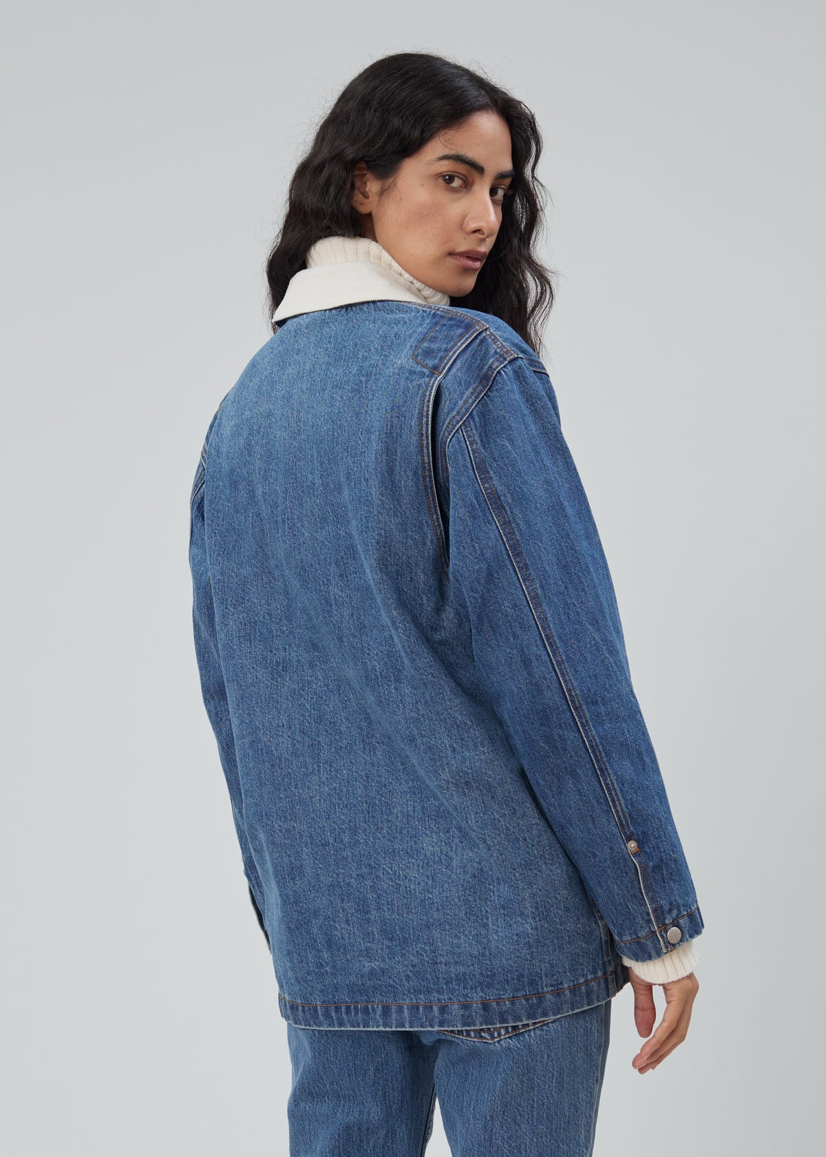 A person viewed from behind, wearing a Barn Jacket in Classic Blue with a light-colored collar over a white turtleneck sweater.