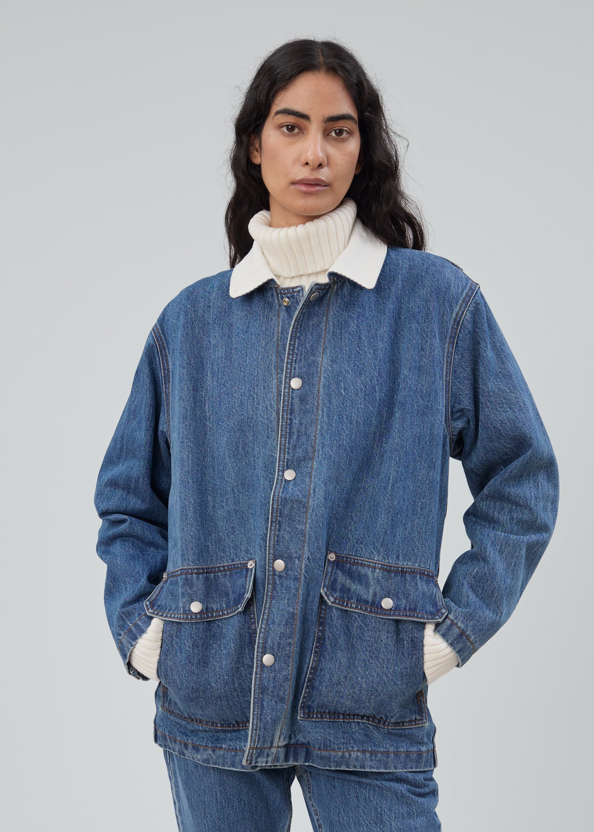 A person wearing a Barn Jacket in Classic Blue with a white collar over a white turtleneck sweater.