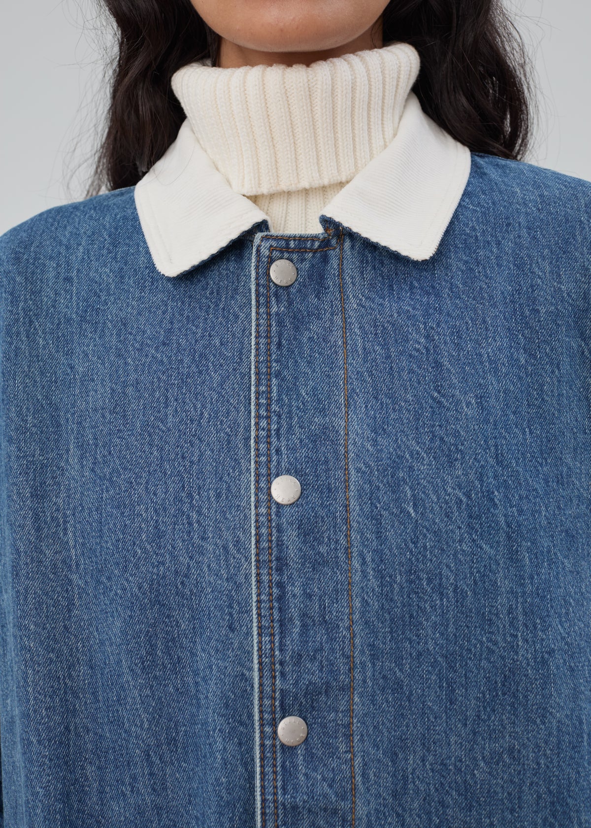 Barn Jacket in Classic Blue made of blue cotton denim with a white corduroy collar, worn over a white ribbed turtleneck sweater.