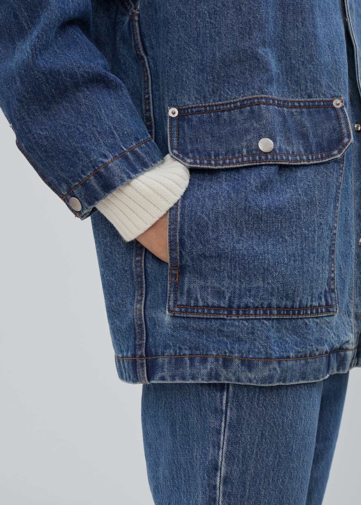 Barn Jacket in Classic Blue made of blue cotton denim with metal buttoned pockets and ribbed white cuffs.