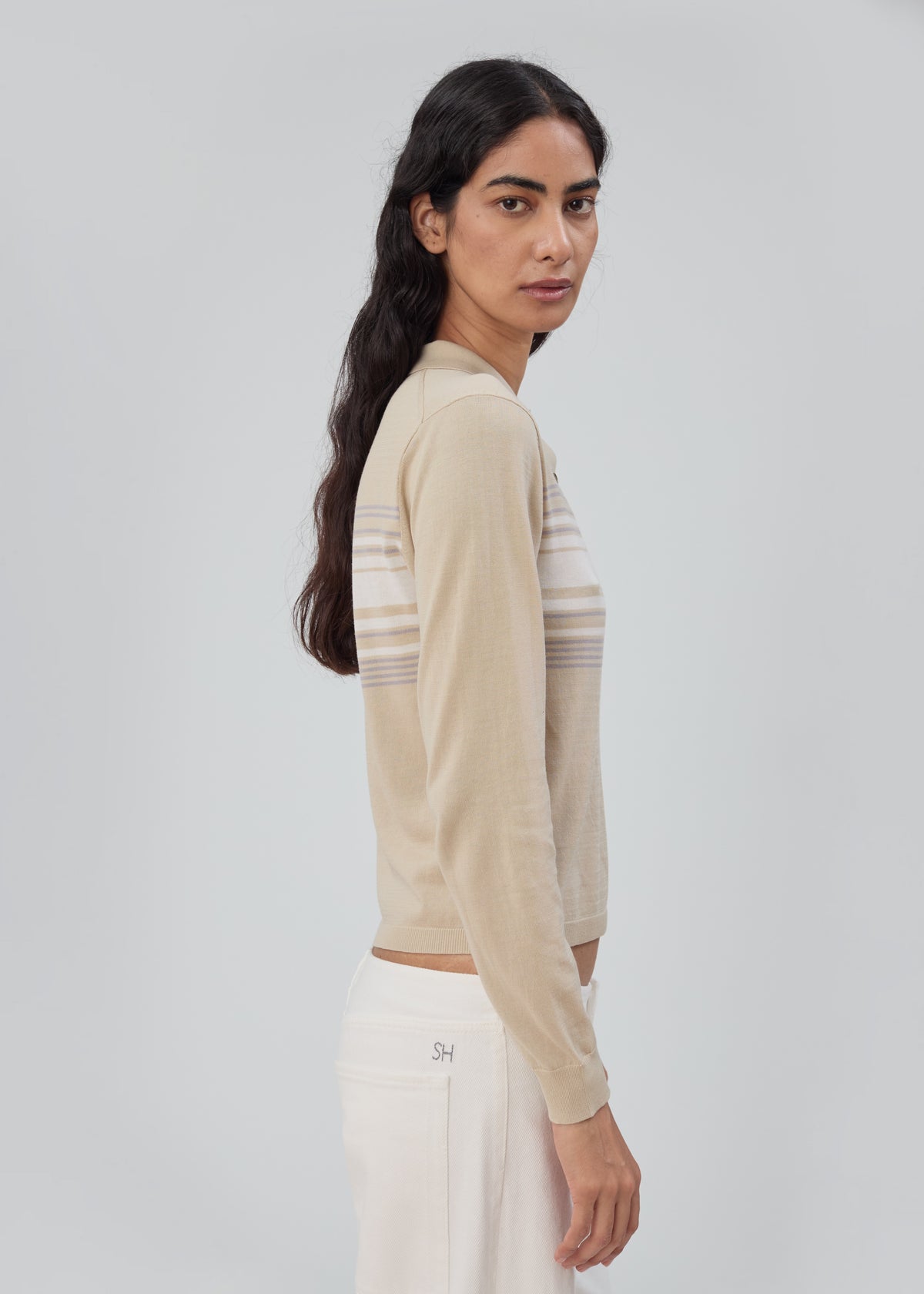 A person wearing a beige, long-sleeve Daughter Sweater Long Sleeve in Beige Stripe with horizontal stripes across the chest and white pants.