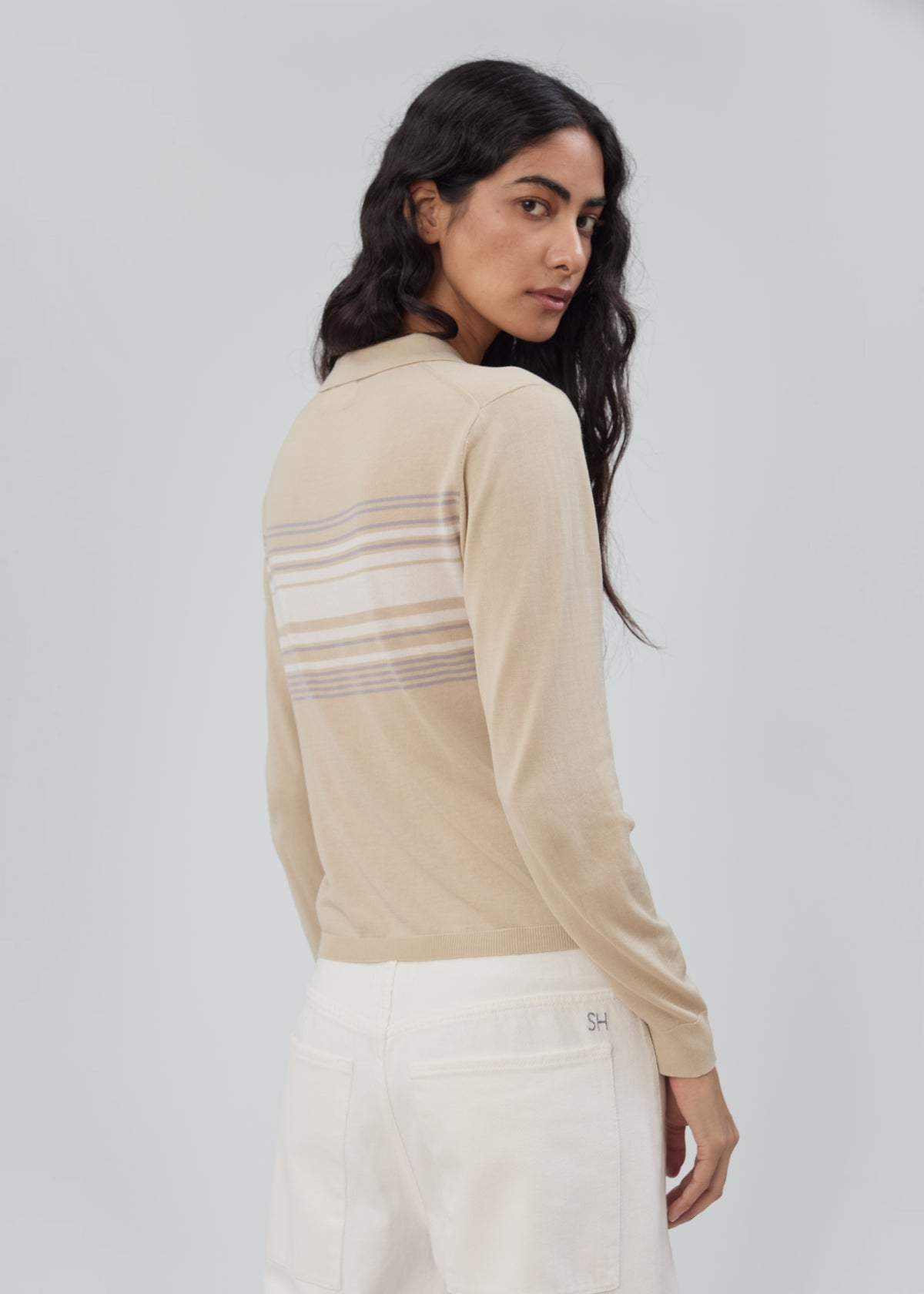 A person wearing a beige, lightweight Daughter Sweater Long Sleeve in Beige Stripe with horizontal stripes across the back.