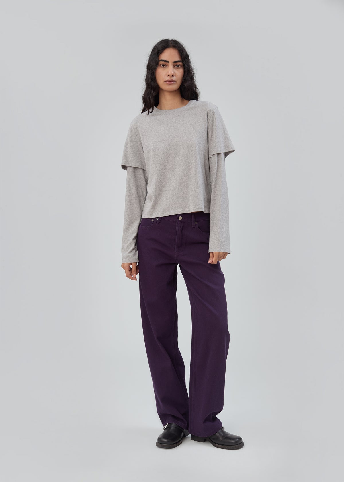 A person wears a grey long-sleeved layered T-shirt with deep purple Everyday Jean in Purple and black shoes.