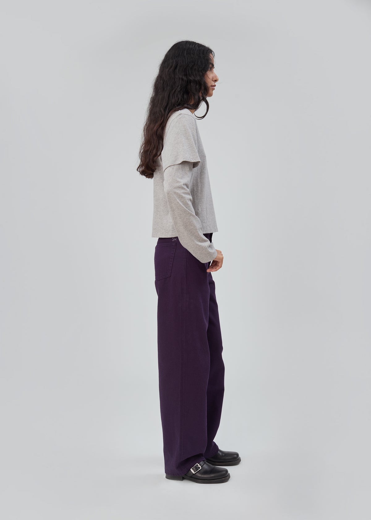 A person viewed from the side wears a grey long-sleeve top, Everyday Jean in Purple, and black buckled shoes.