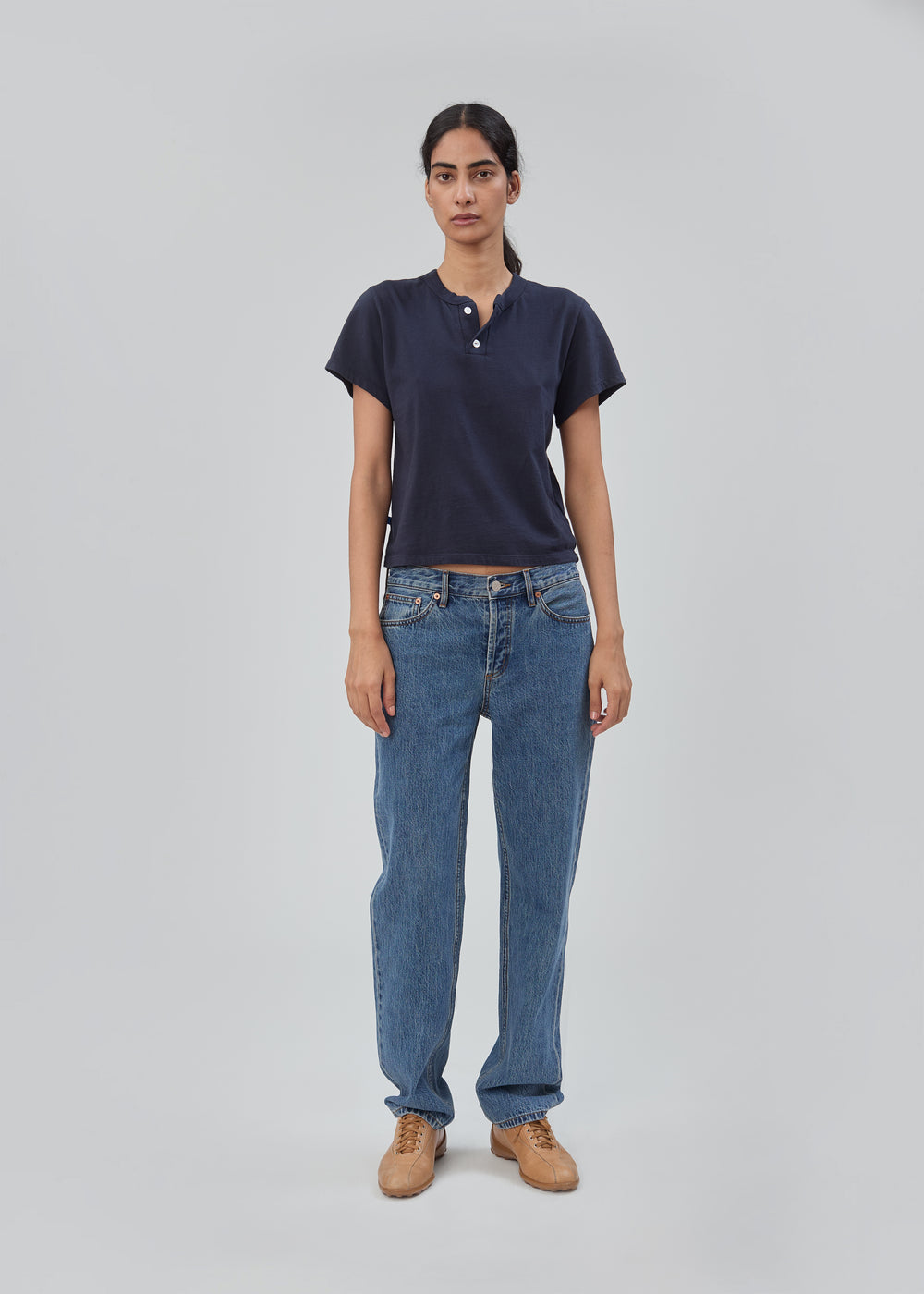 A person wearing a dark blue short-sleeved henley shirt, Life Jean in Classic Blue, and tan shoes.