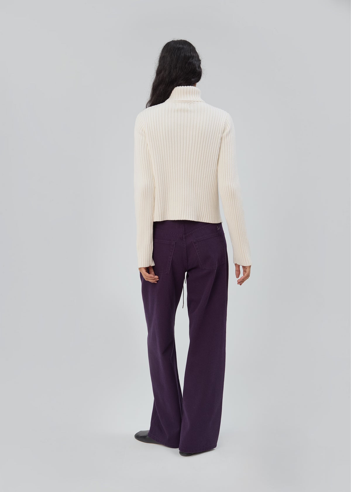 Back view of a person wearing a cream ribbed turtleneck sweater and purple Cool Jean in Purple with a relaxed leg.
