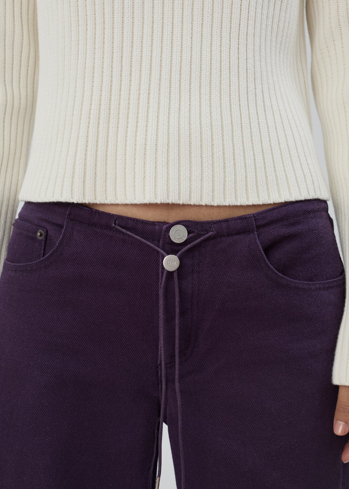 Cool Jean in Purple featuring a low-rise, relaxed leg, central drawstring, and silver-tone hardware, worn with a cream ribbed sweater.