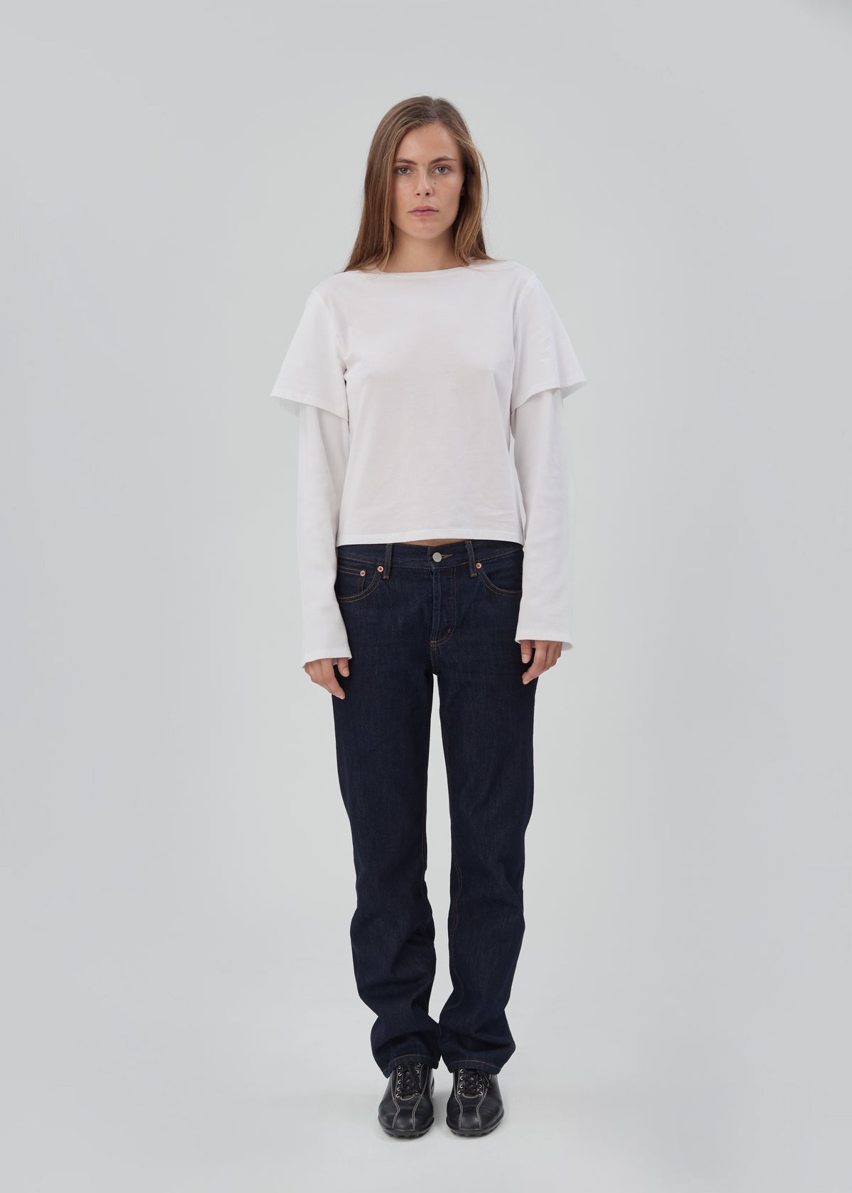 A person wearing a white long-sleeve layered top and Life Jean in Indigo Indigo with black shoes.