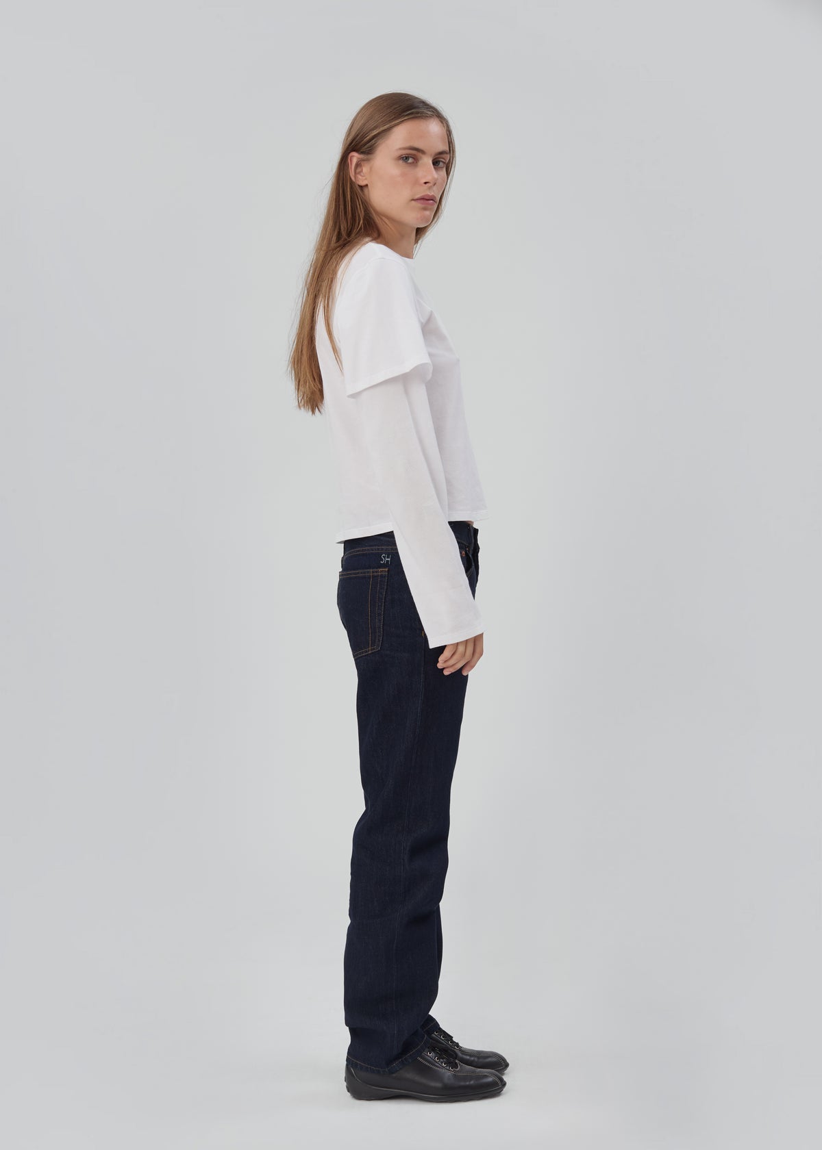 A woman wearing a white long-sleeve t-shirt and Life Jean in Indigo Indigo, featuring a dark indigo five-pocket straight-leg design.