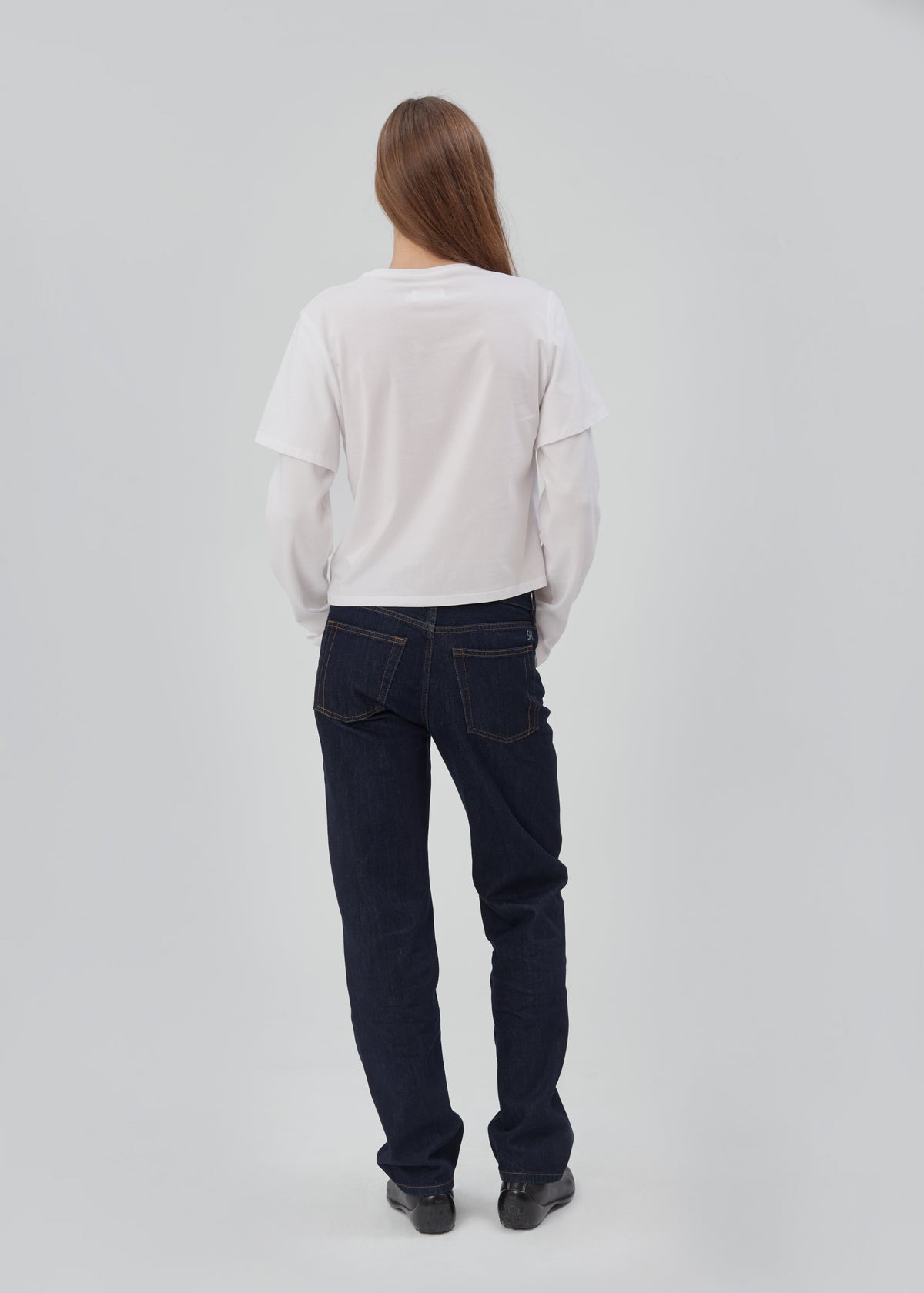 Back view of a person wearing a white long-sleeve T-shirt and Life Jean in Indigo Indigo straight-leg jeans.