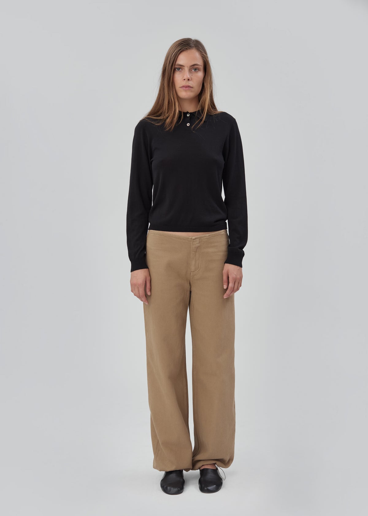A woman wears a black Daughter Sweater Long Sleeve in a lightweight knit with a button-up collar and tan wide-leg trousers.