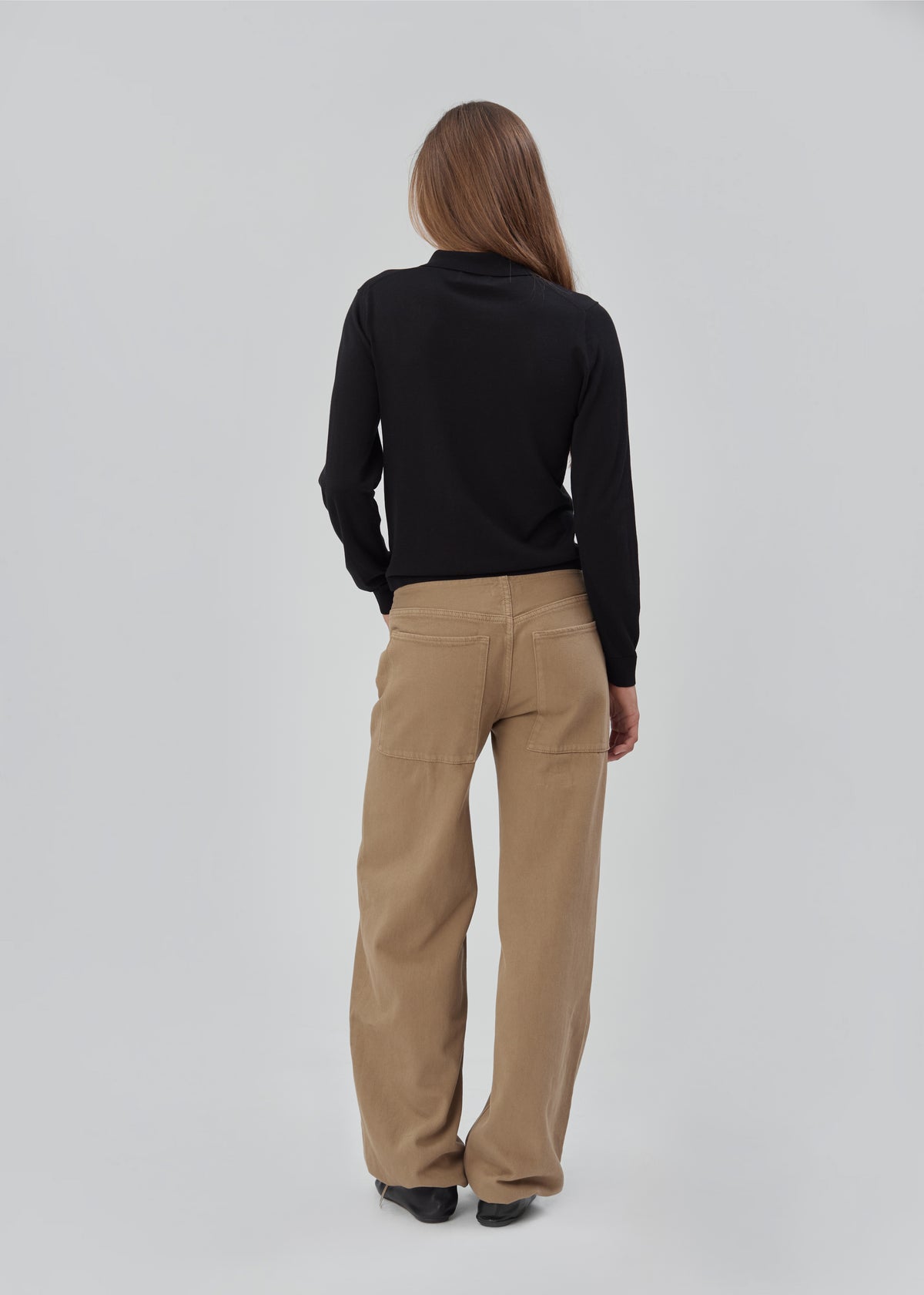A person seen from behind, wearing a Daughter Sweater Long Sleeve in Black and wide-leg tan pants.