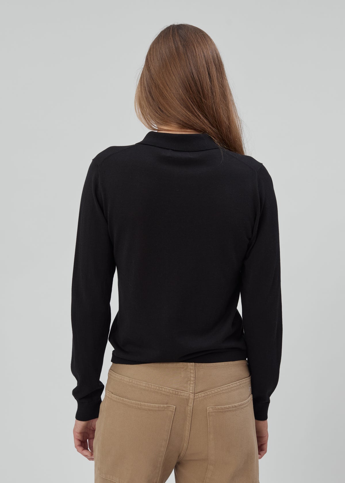 A person viewed from behind wearing a black Daughter Sweater Long Sleeve in tan pants.