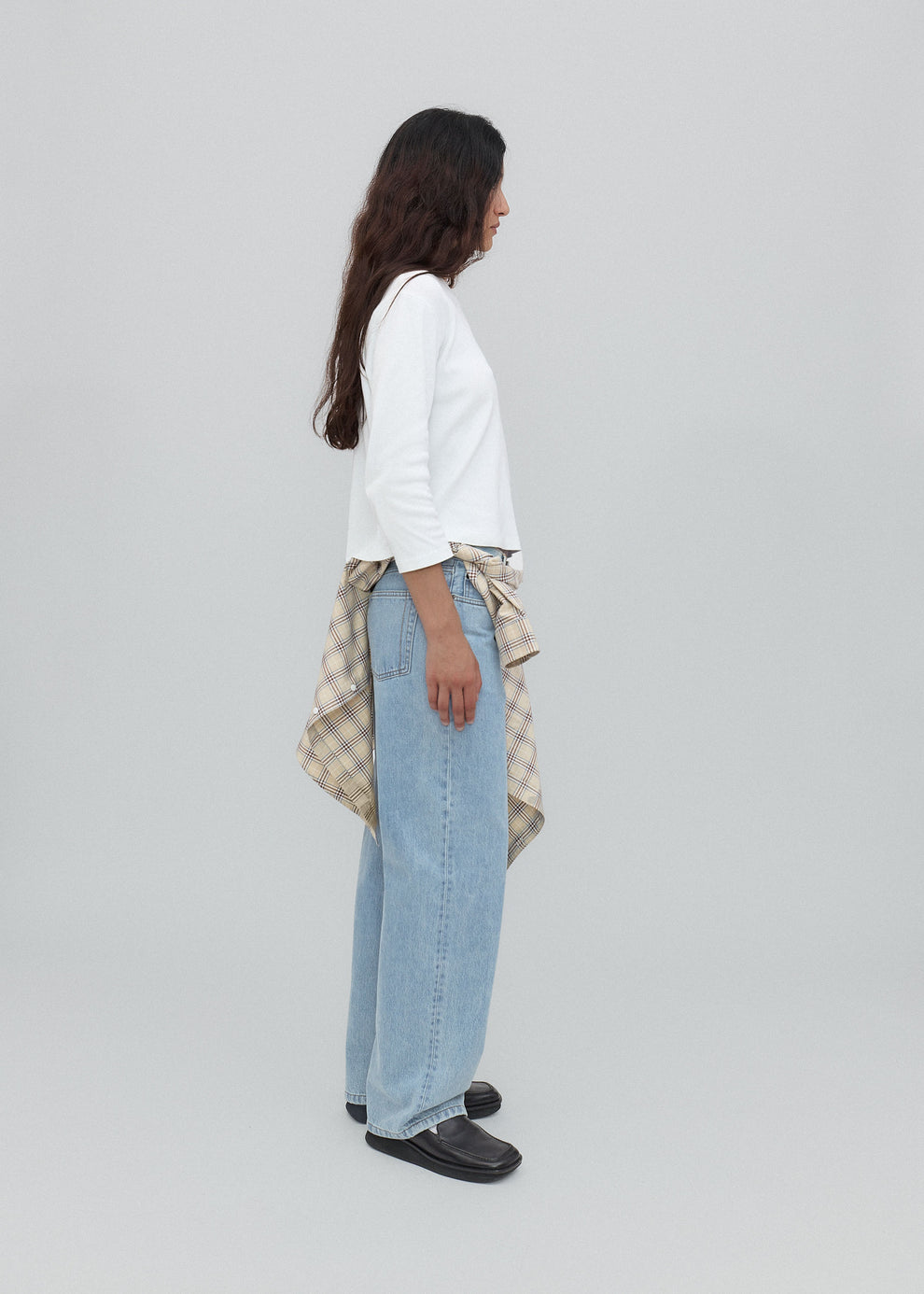 Person wearing a white shirt, light blue jeans, and black shoes on a plain background