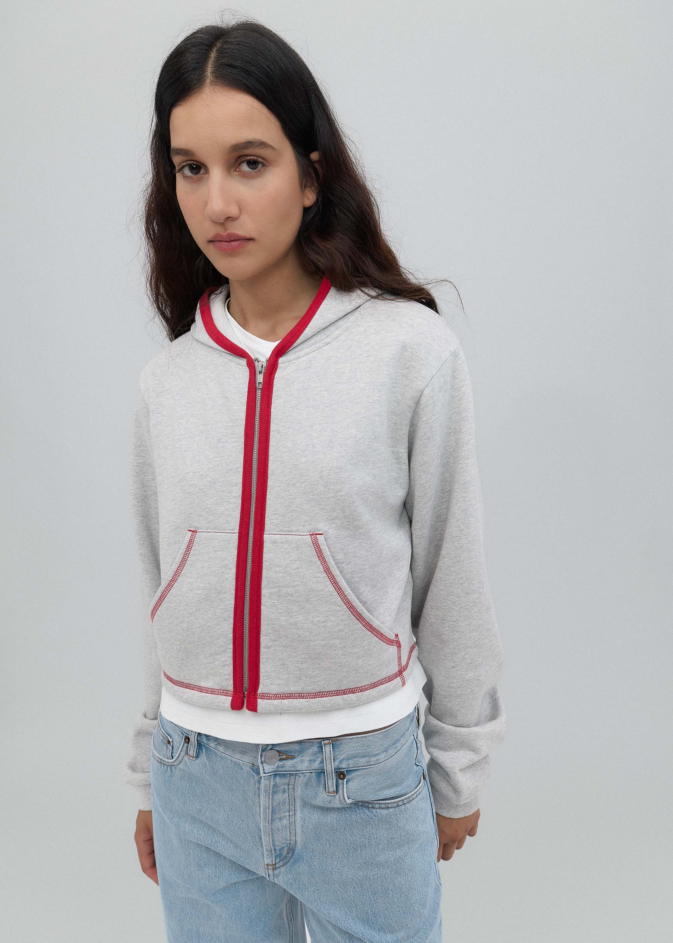 Woman wearing a gray hoodie with a red zipper on a plain background