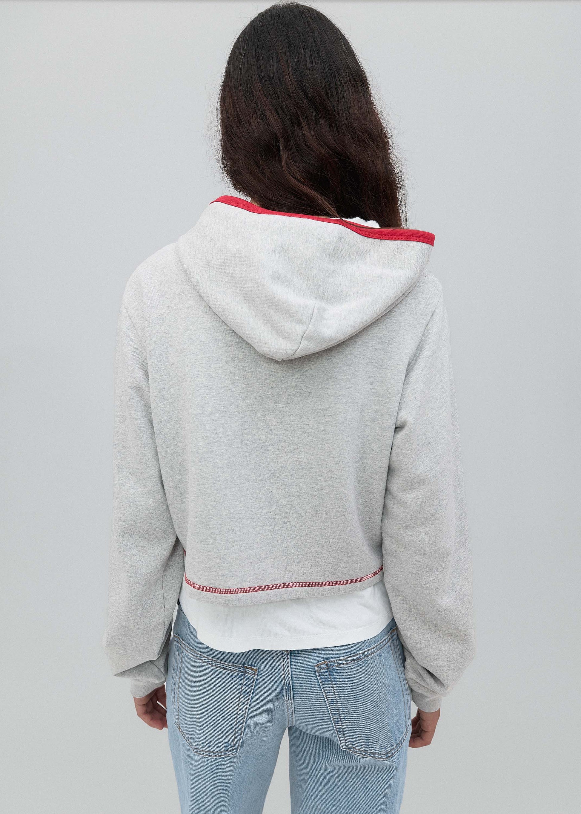 Person wearing a gray hoodie with red trim on a plain background