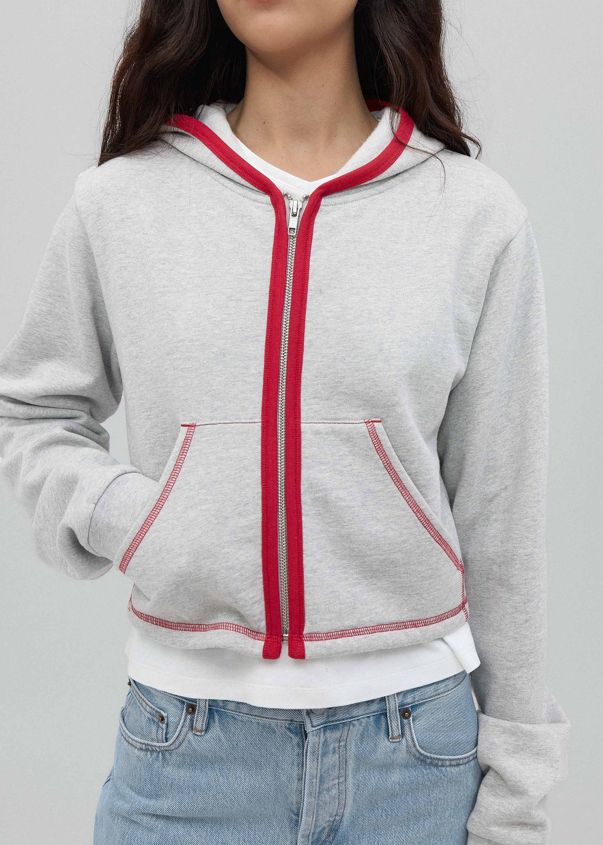 Gray hoodie with red zipper and trim worn by a person on a plain background