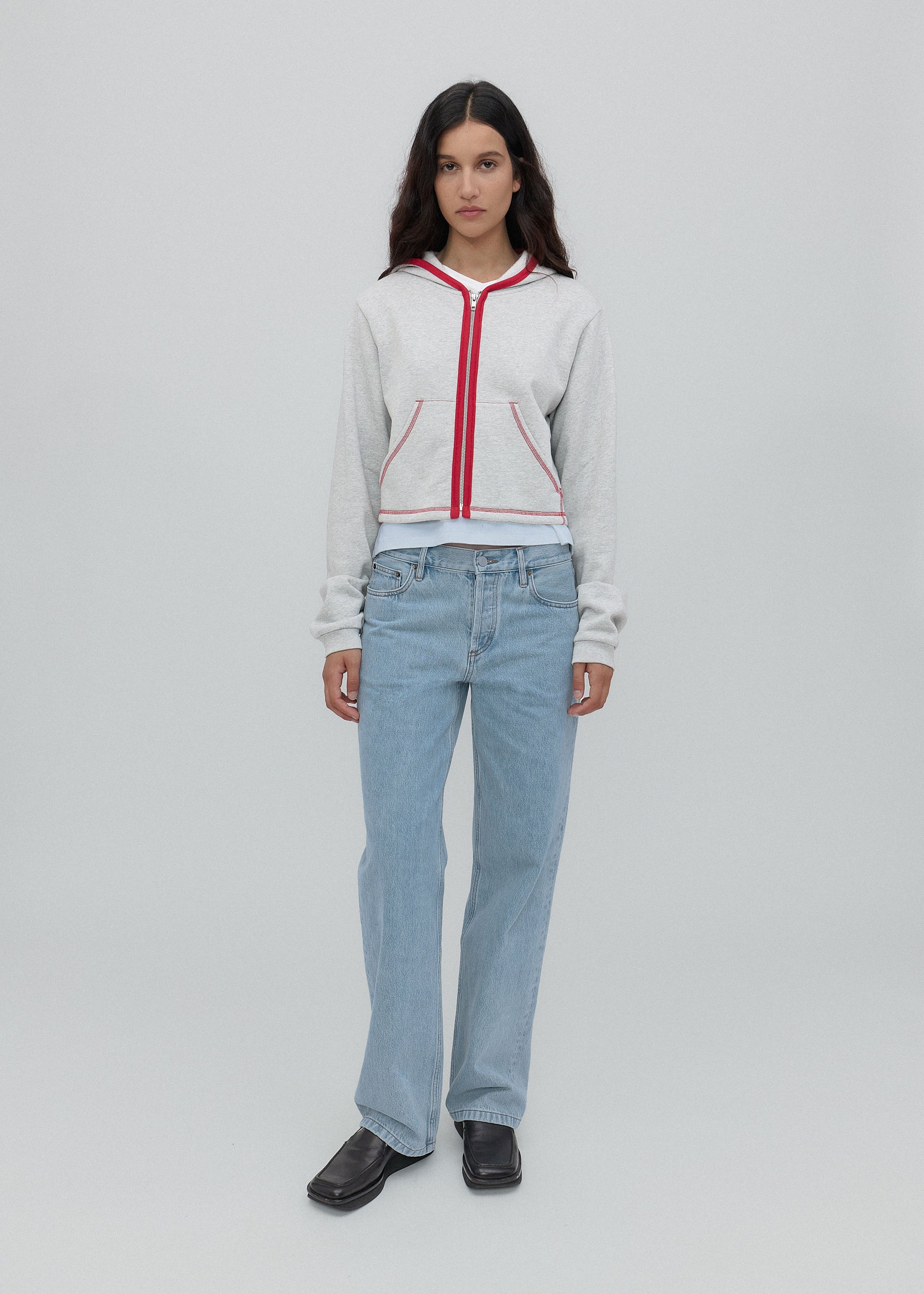 Woman wearing a light gray hoodie with red accents and light blue jeans on a white background