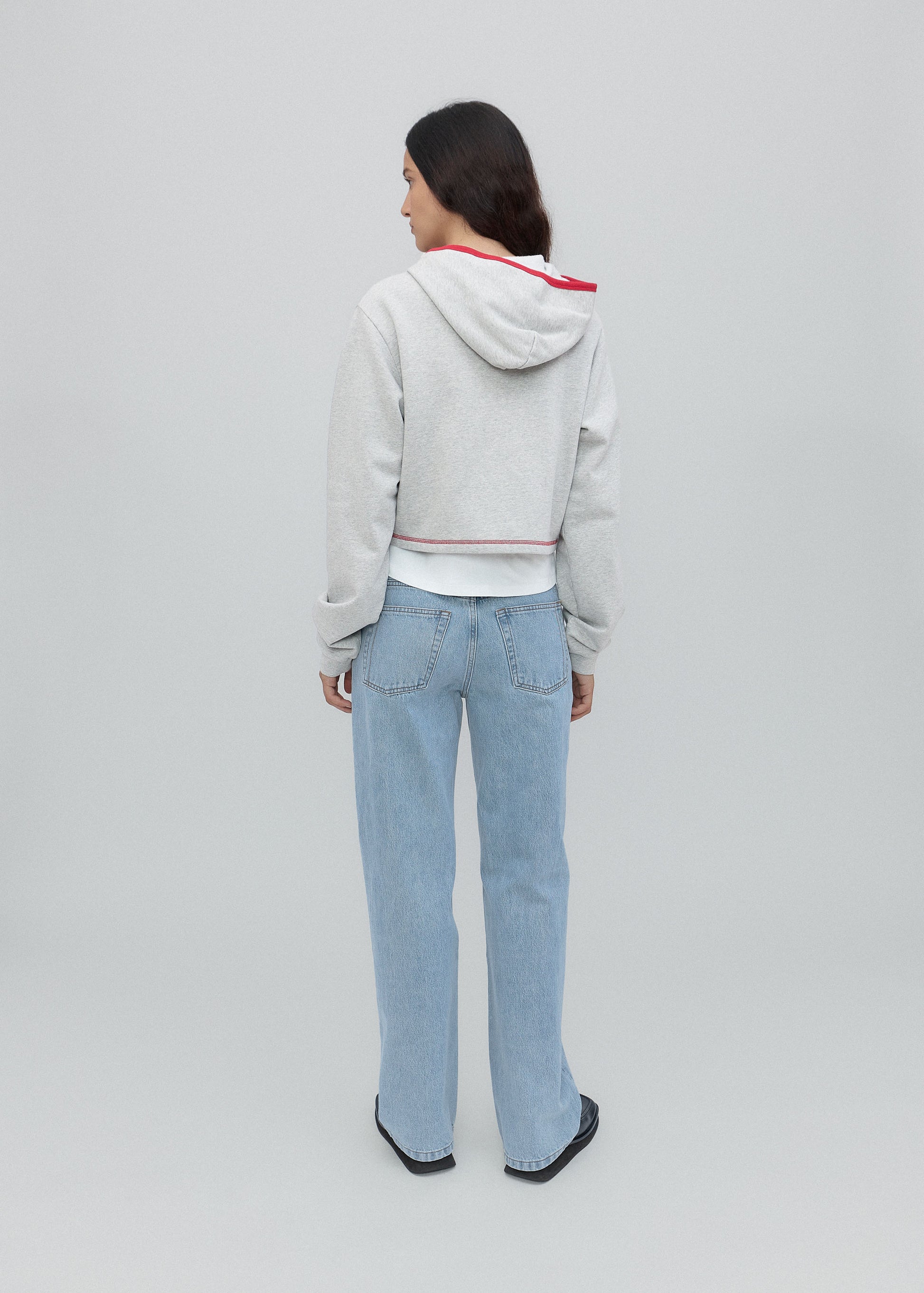 Person wearing a light gray hoodie and blue jeans on a plain background