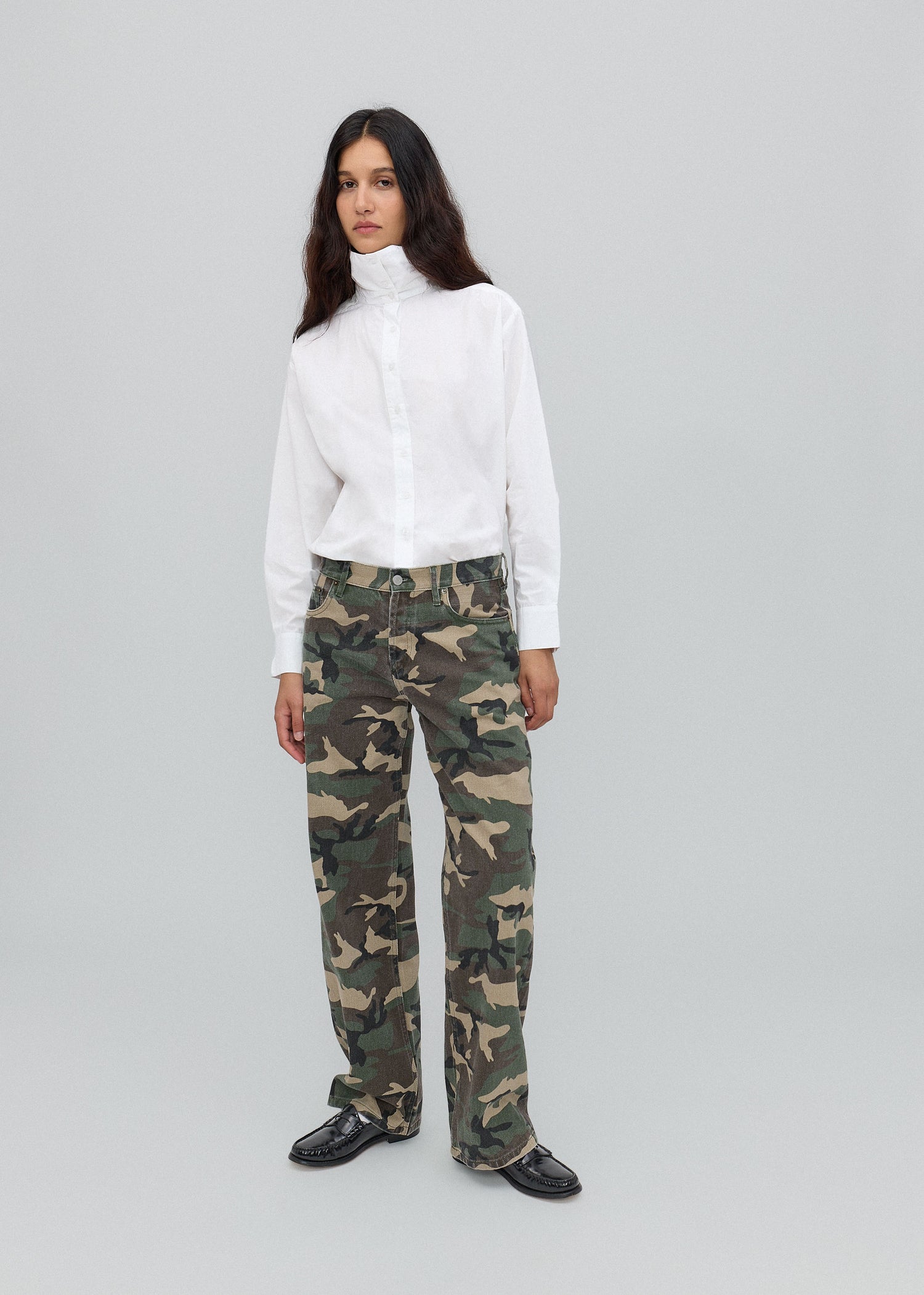 Person wearing a white turtleneck and camouflage pants on a light gray background
