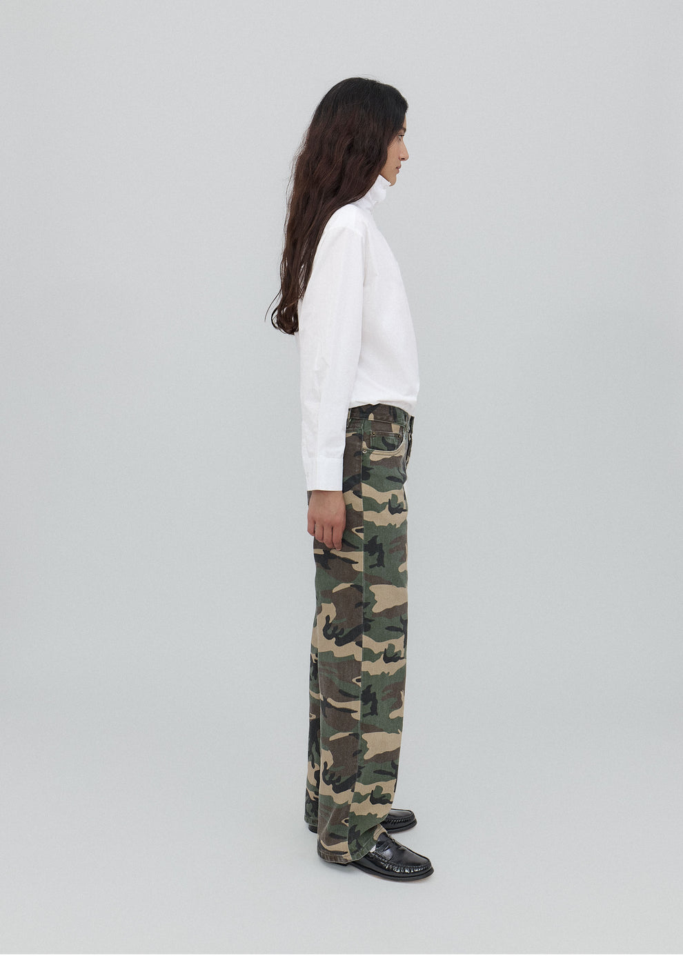 Person wearing camouflage pants and a white top on a light gray background