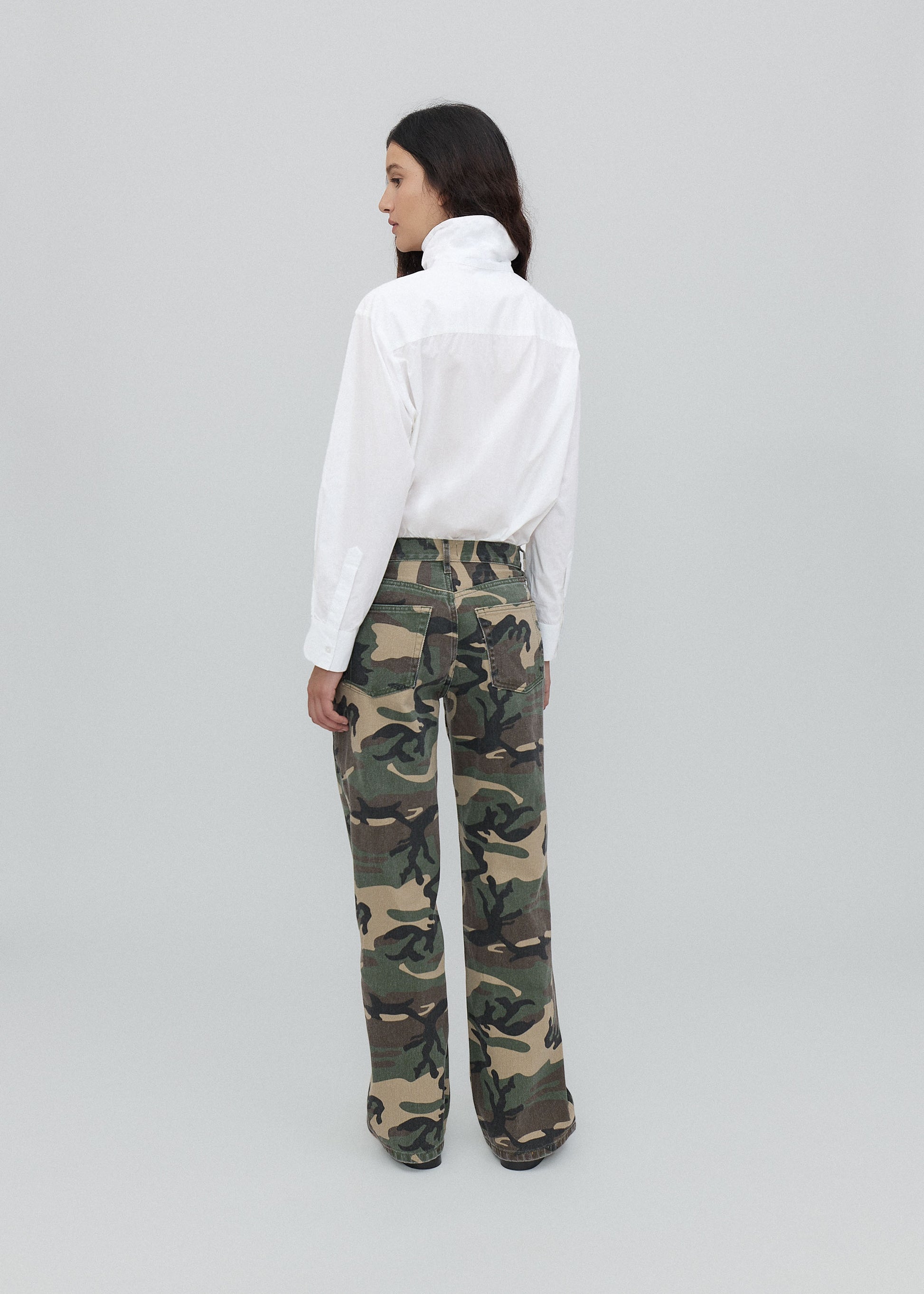 Person wearing a white shirt and camouflage pants on a light gray background