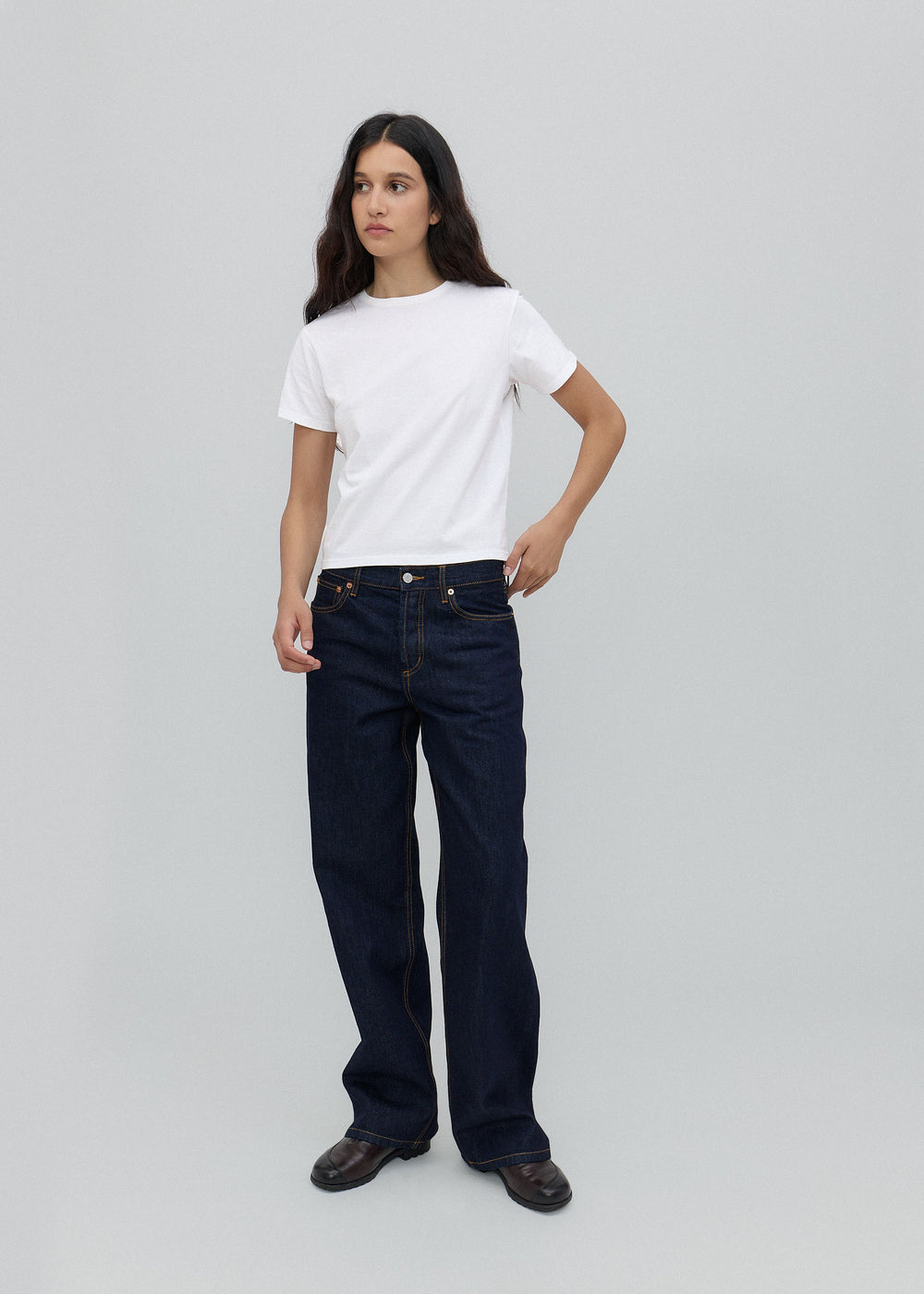 Person wearing a white t-shirt and dark jeans on a light gray background