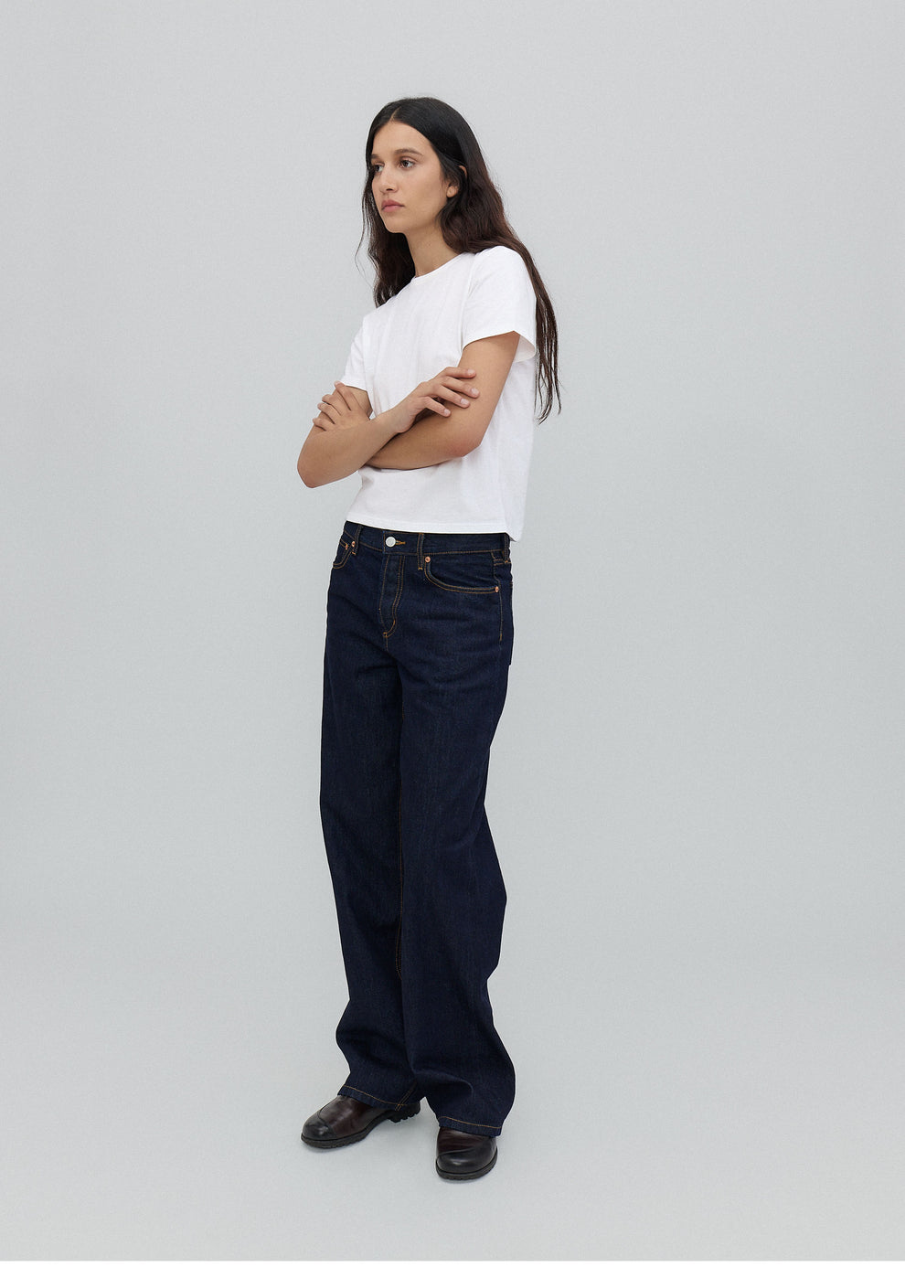 Woman wearing a white t-shirt and dark blue jeans on a light gray background