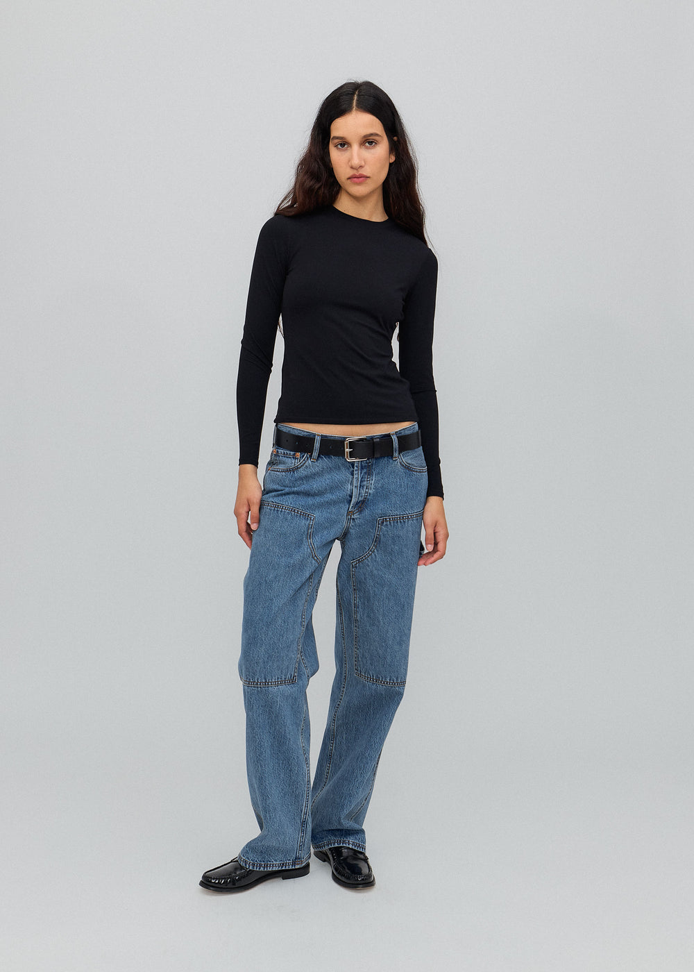 Person wearing a black long-sleeve top and blue jeans on a gray background