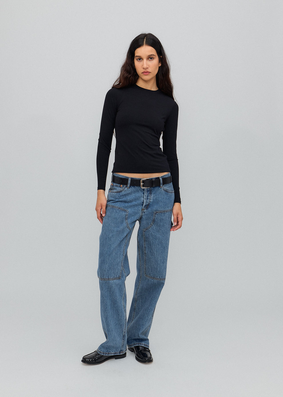 Person wearing a black long-sleeve top and blue jeans on a gray background