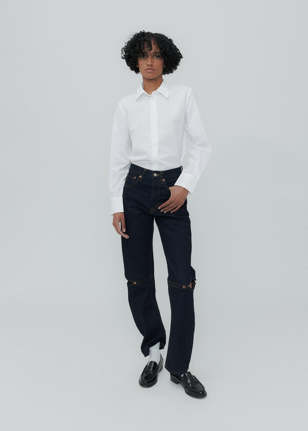 Person wearing a white shirt and dark jeans on a light gray background