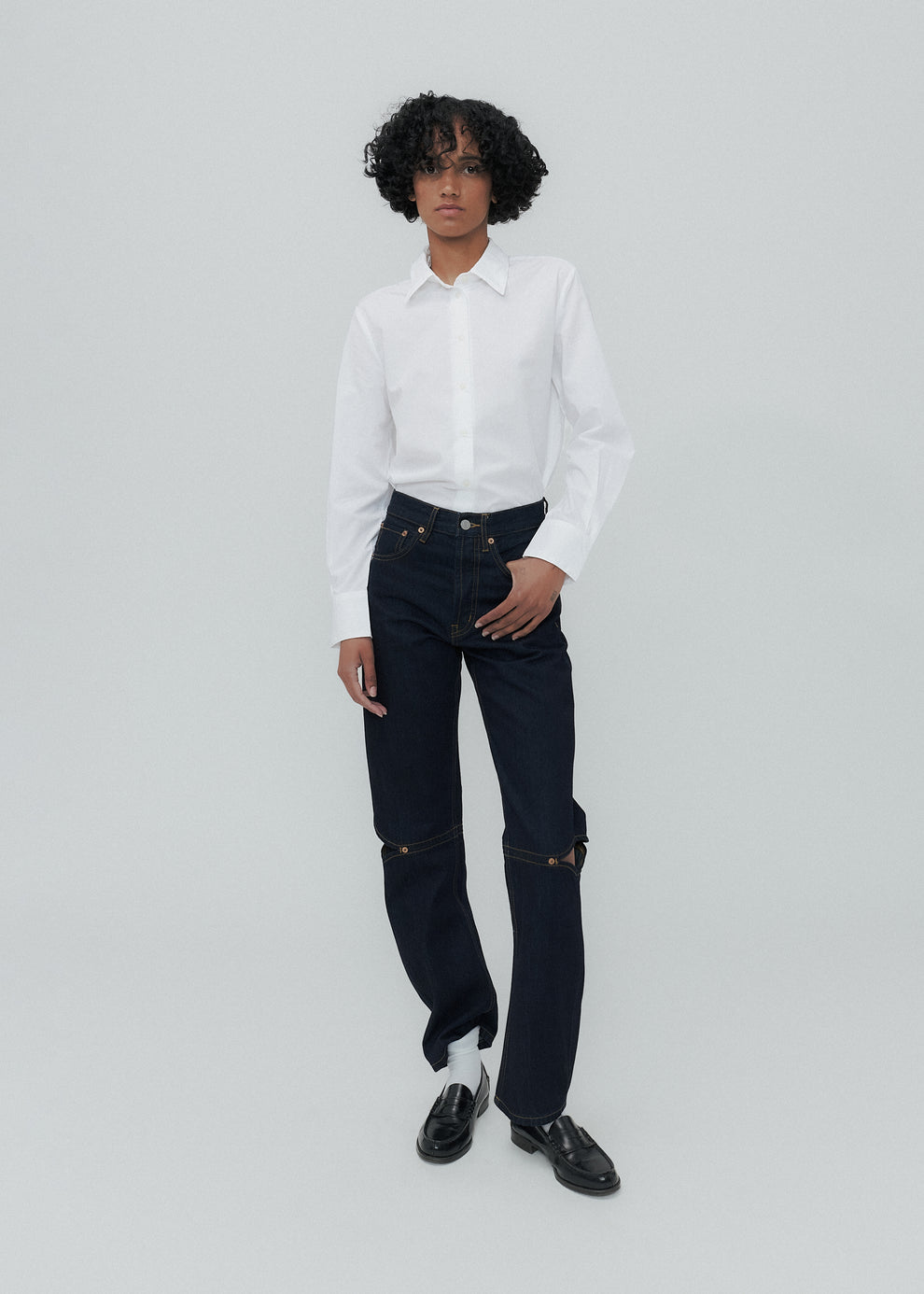 Person wearing a white shirt and dark jeans on a light gray background