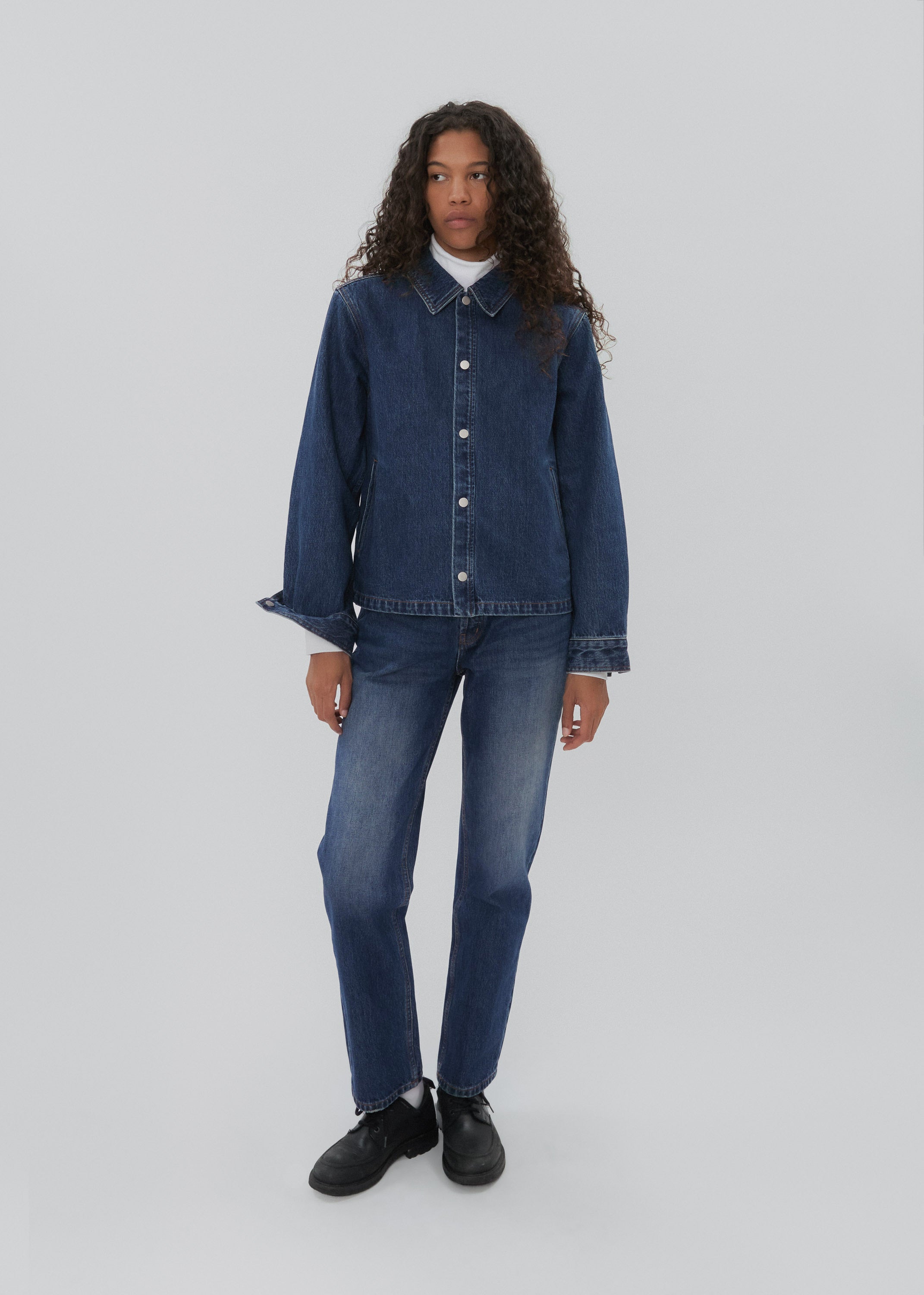 Person wearing a blue denim jacket and jeans on a white background