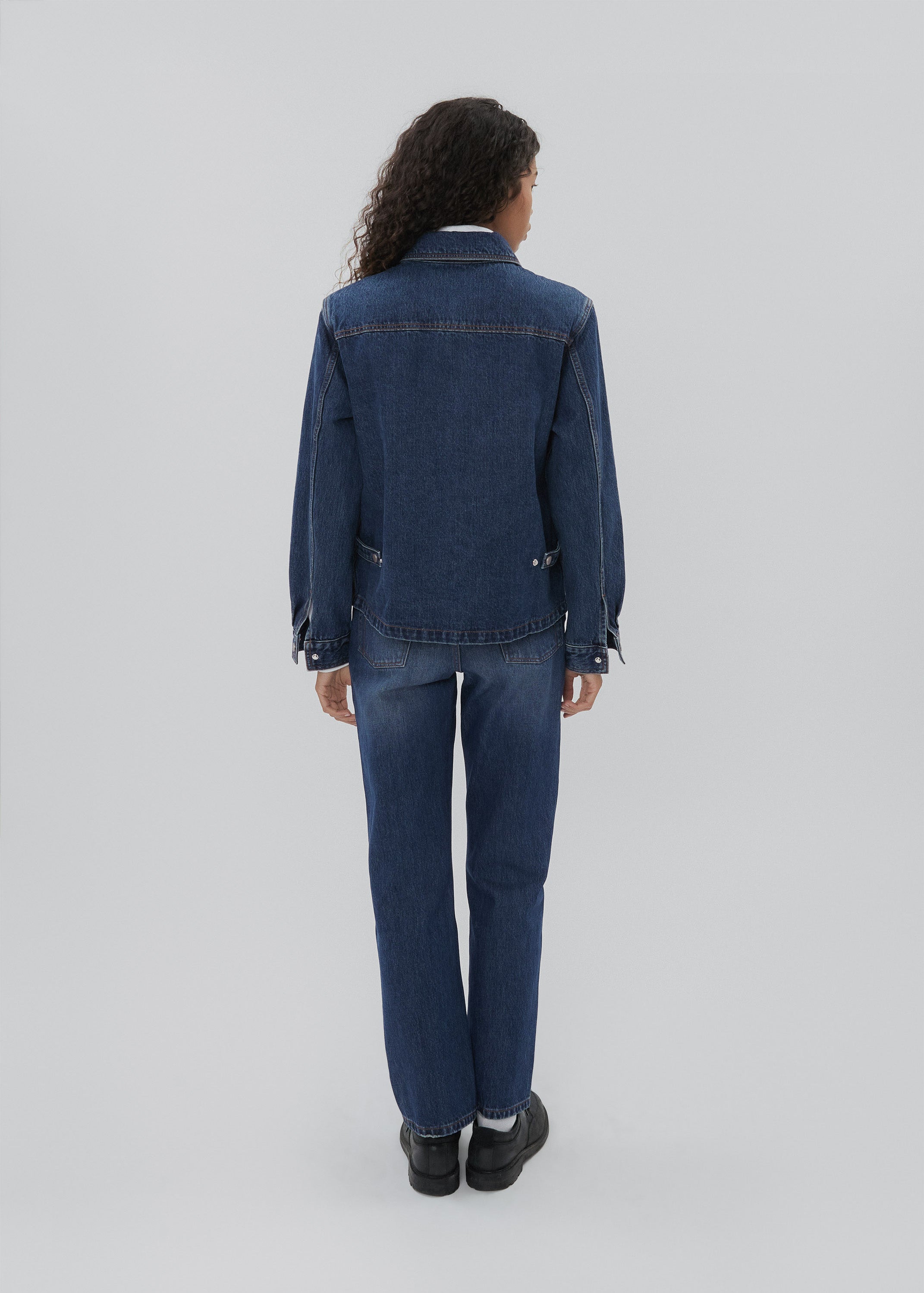 Person wearing a blue denim jacket and pants on a white background