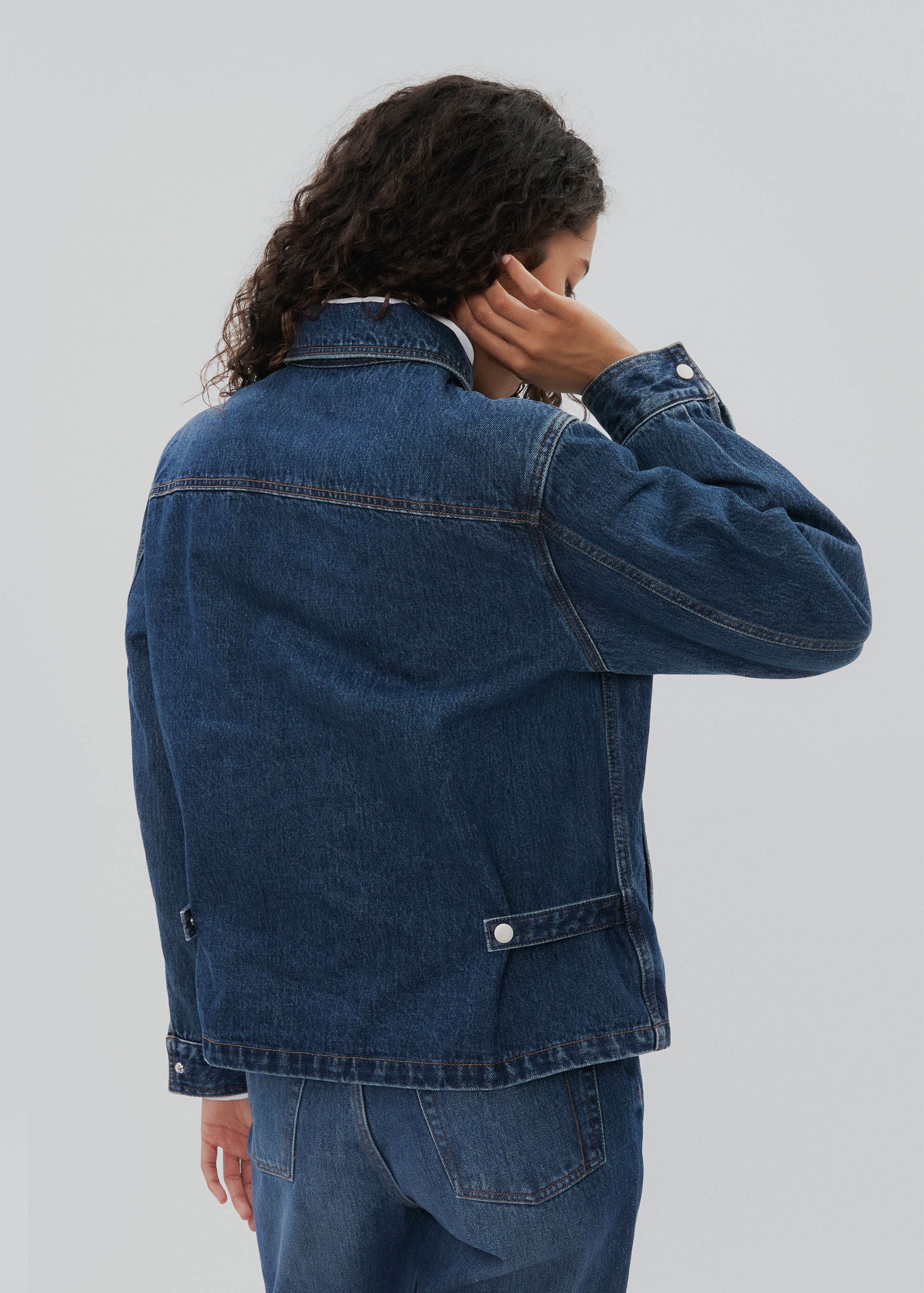 Person wearing a blue denim jacket on a plain background