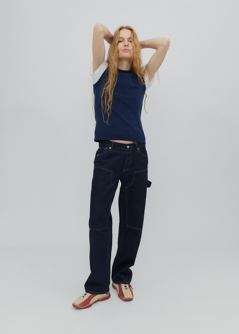 Person wearing a navy blue sleeveless top and jeans on a white background