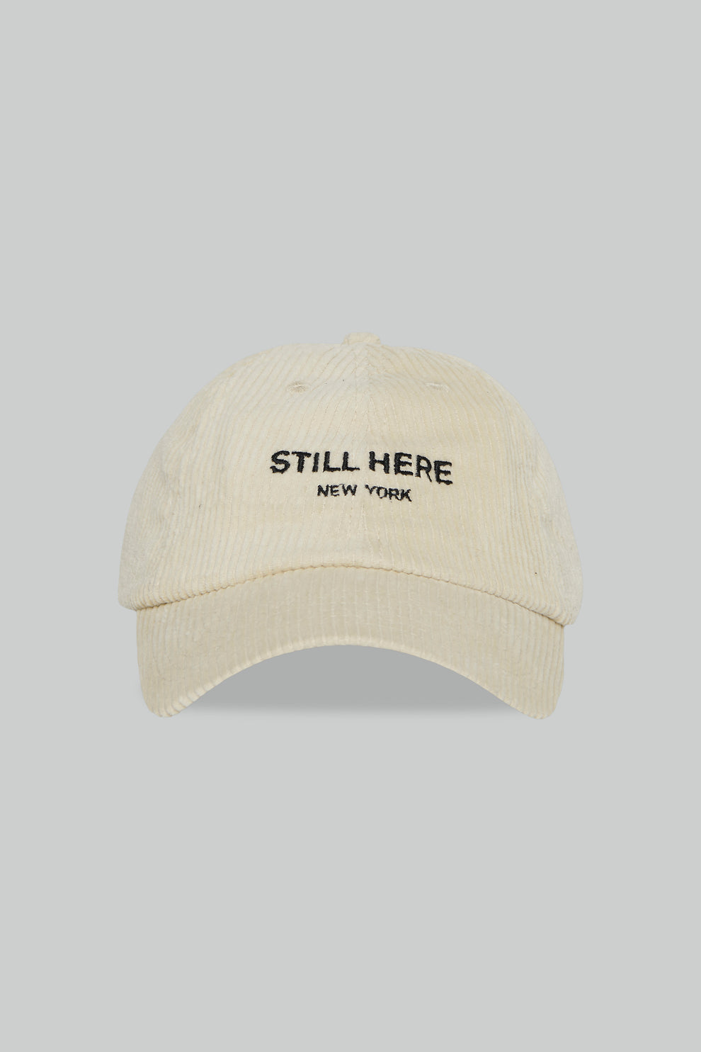 Beige cap with 'STILL HERE New York' text on a gray background