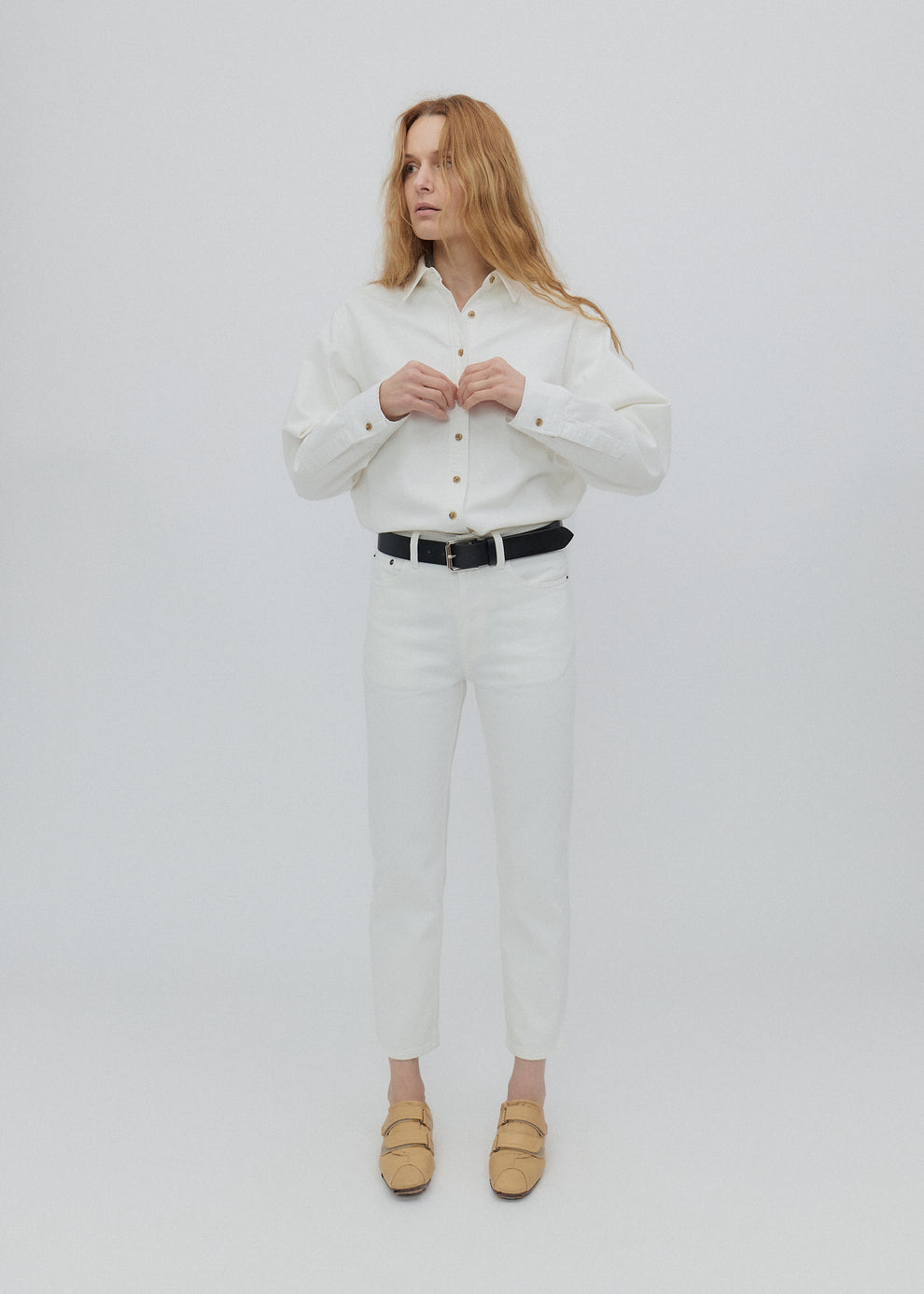 Woman wearing a white shirt and pants with a black belt on a light gray background