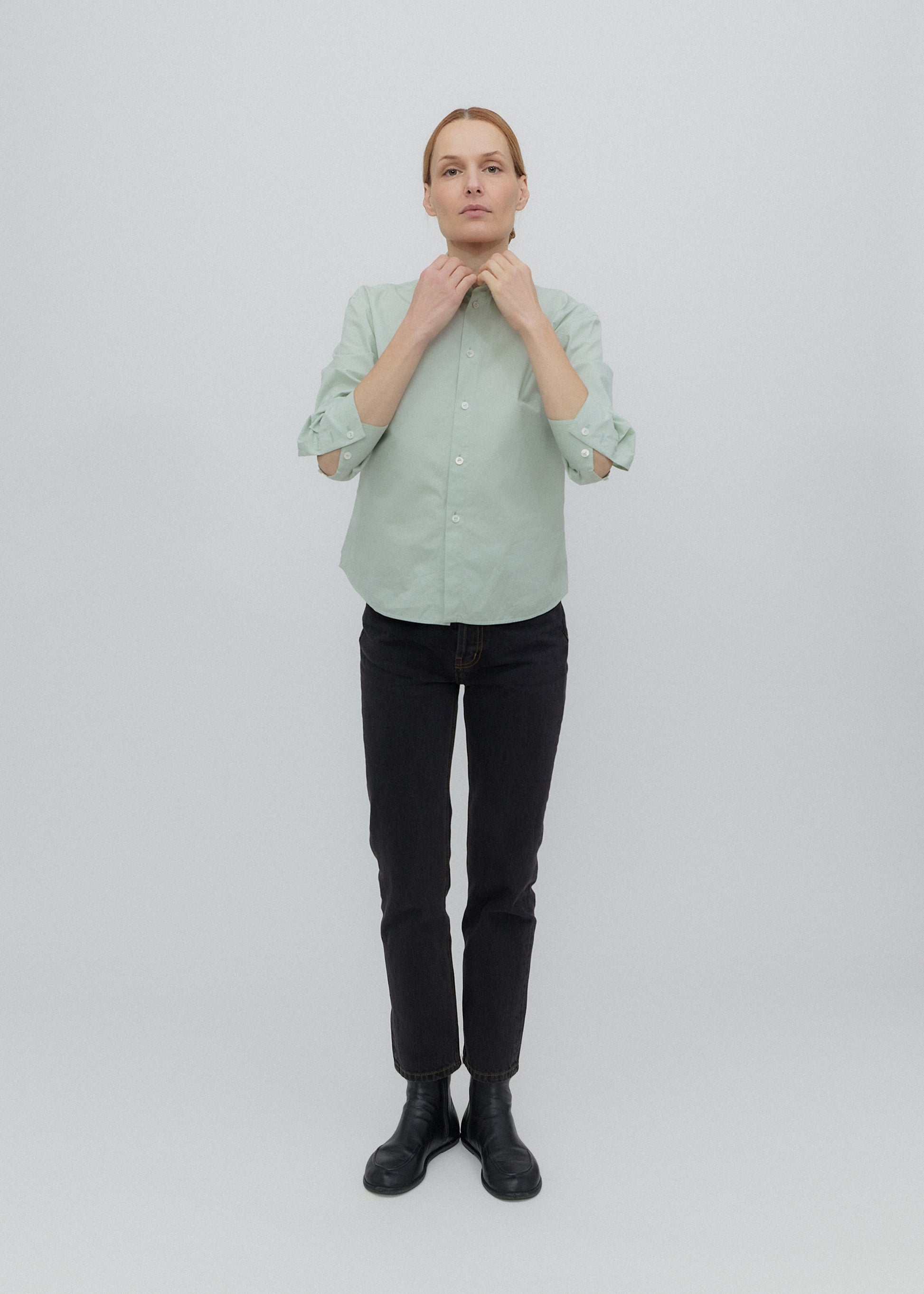 Person wearing a light green shirt and black pants on a white background